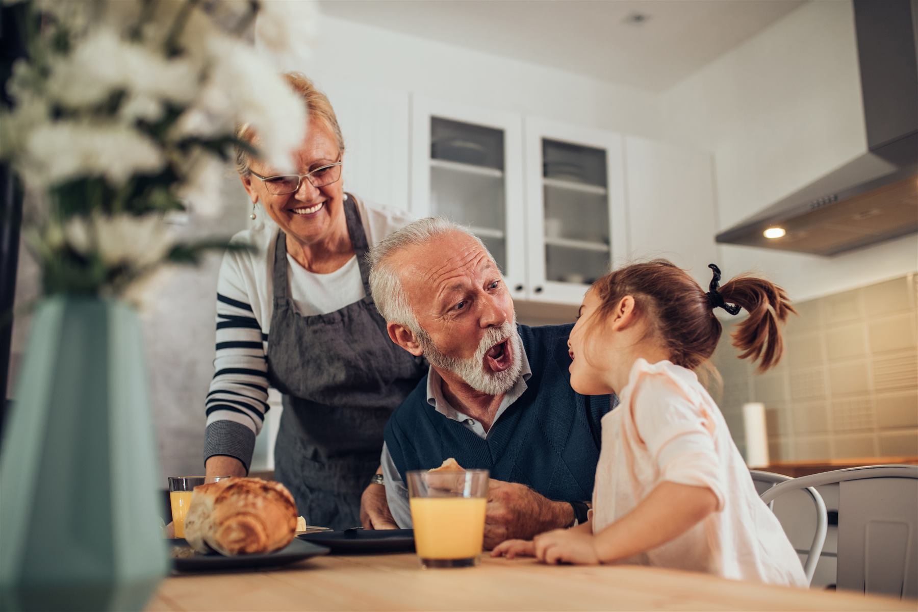 Due nonni e la nipotina ridono insieme a colazione in cucina
